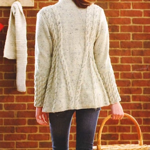 May include: A white cable knit sweater with a speckled pattern. The sweater has a high neckline and long sleeves. The model is wearing blue jeans and holding a wicker basket.