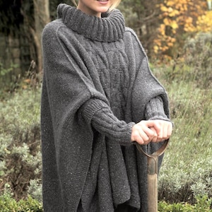 Peut inclure: Un poncho en tricot gris avec un motif en tricot torsadé et un col roulé. Le poncho a des manches longues et est porté avec un jean bleu. La personne tient un outil de jardinage.