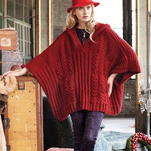 May include: A woman wearing a red knitted poncho with a hood and a matching red hat. The poncho has a cable knit design and is paired with patterned purple leggings. The image is set in a vintage-style room.