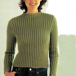 May include: A green ribbed knit sweater with long sleeves. The sweater has a high neckline and is paired with dark blue jeans. Sunglasses are perched on the model's head.