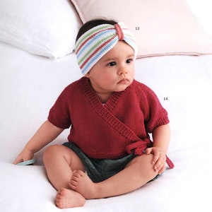 May include: A baby wearing a red knitted wrap top with a white and green striped headband. The headband has a bow on top. The baby is sitting on a white surface.
