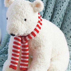 Peut inclure: Ours en peluche blanc portant une écharpe rayée rouge et blanche. L'ours est assis sur une couverture en crochet bleu et blanc.