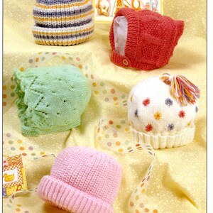 May include: Five knitted baby hats in different colours and styles. The hats are on a yellow background with a white polka dot ribbon.