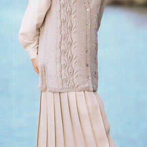 May include: A beige knitted waistcoat with a cable knit pattern and button fastening. The waistcoat is worn over a white button-down shirt and a beige pleated skirt.