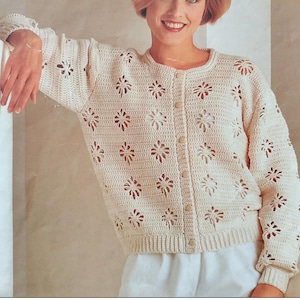 May include: Cream-colored crochet cardigan with a floral pattern. The long-sleeved sweater features a round neckline, button-up front, and ribbed cuffs and hem. The openwork design creates a delicate, airy look, perfect for layering.