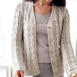Könnte beinhalten: Ein beigefarbener Strickcardigan mit einem Zopfmuster und einem Knopfverschluss. Der Cardigan hat einen V-Ausschnitt und lange Ärmel.