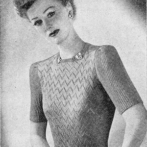 May include: A black and white photo of a woman wearing a knitted sweater with a chevron pattern. The sweater has a round neckline and short sleeves.
