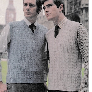 Puede incluir: Dos hombres con chalecos de punto de cuello en V. El chaleco de la izquierda es azul y el de la derecha es gris. Ambos hombres llevan camisas blancas con corbatas.