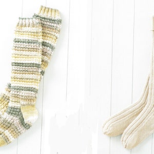 May include: Two pairs of knitted knee-high socks. One pair is striped in beige, green, and white. The other pair is solid beige.
