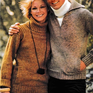 May include: A couple wearing matching turtleneck sweaters. The woman is wearing a brown sweater with a long pendant necklace. The man is wearing a gray sweater with a white turtleneck underneath. He is wearing a brown hat.
