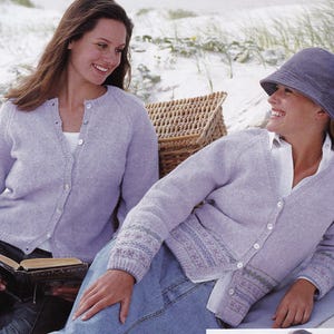 Op de afbeelding: Twee vrouwen dragen lichtpaarse vesten. De vrouw links houdt een boek vast en de vrouw rechts draagt een blauwe denim rok en een hoed.