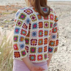 May include: A cream-colored, short-sleeved crochet jacket featuring a patchwork design of colorful squares. The squares are in shades of pink, blue, orange, and green. The jacket is worn over a light pink top.