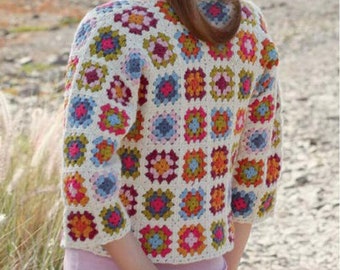 Könnte beinhalten: Eine cremefarbene, kurzärmelige Häkeljacke mit einem Patchwork-Design aus bunten Quadraten. Die Quadrate sind in den Farbtönen Rosa, Blau, Orange und Grün gehalten. Die Jacke wird über einem hellrosa Oberteil getragen.