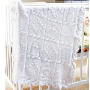 May include: White knitted baby blanket with a crocheted border. The blanket features a variety of textured patterns, including squares, circles, and diamonds.