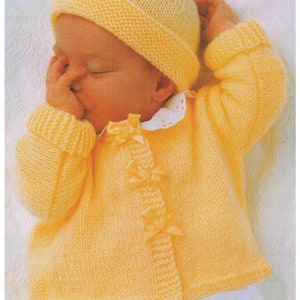 May include: A yellow knitted baby cardigan with a matching hat. The cardigan has a button fastening and a bow detail on the front.