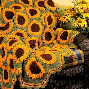 Może przedstawiać: Ręcznie robiony pled w kształcie słonecznika w odcieniach zieleni, brązu i żółci. Pled jest położony na wiklinowym krześle z poduszką w kratę.