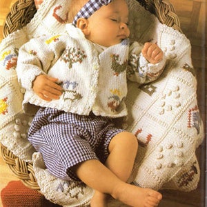 May include: A baby wearing a white knitted cardigan with a colourful floral design, blue and white checked trousers, and a white and blue checked headband, sleeping in a wicker basket lined with a white knitted blanket.