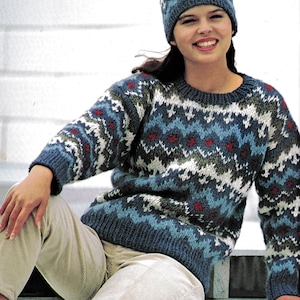 Könnte beinhalten: Ein Strickpullover und ein passendes Mützen-Set. Der Pullover und die Mütze weisen ein geometrisches Muster in Blau-, Weiß-, Rot- und Grüntönen auf. Der Pullover hat einen Rundhalsausschnitt und lange Ärmel. Die Mütze ist eine eng anliegende Beanie.
