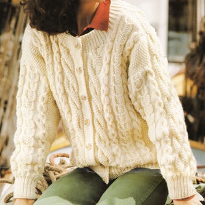 Könnte beinhalten: Ein cremefarbener Strickpullover mit Zopfmuster, Knopfleiste und langen Ärmeln.