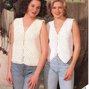 May include: Two women wearing white crocheted sleeveless vests with button closures. The vests have a delicate openwork pattern. The women are wearing blue jeans.