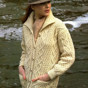 May include: A cream-colored cable knit cardigan with a brown felt hat. The cardigan has a button-up front and two pockets. The hat has a wide brim and a simple design.