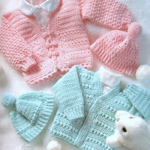 May include: Two crocheted baby sweaters and hats. One set is pink and the other is light blue. Both sets have a button closure and a pom-pom on the hat.