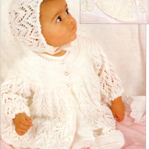 May include: A white knitted baby outfit with a lace pattern. The outfit includes a bonnet, cardigan, and booties. The outfit is laid out on a pink surface. 4 PLY