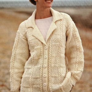 May include: A cream-coloured knitted cardigan with a cable knit pattern and button fastening. The cardigan has a collar and long sleeves.