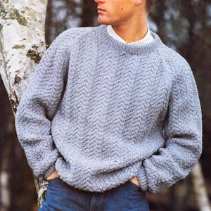 Puede incluir: Un suéter de punto azul claro con un patrón de chevron. El suéter tiene cuello redondo y mangas largas.