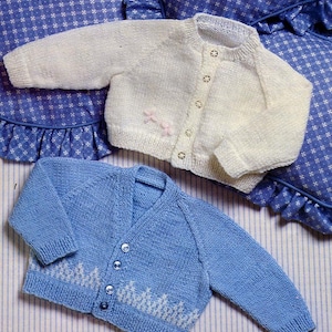 May include: Two knitted baby cardigans, one white and one blue. The white cardigan has a button closure and pink embroidered flowers. The blue cardigan has a button closure and a white embroidered design.