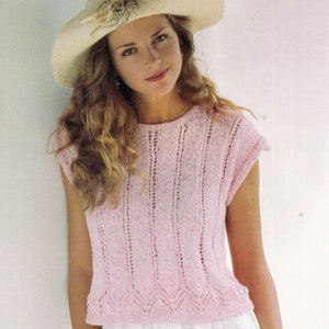 Puede incluir: Un top de crochet rosa con un delicado patrón de calado. El top tiene un escote redondo y mangas cortas. La modelo lleva un sombrero blanco.