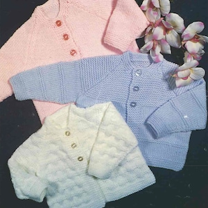 May include: Three knitted baby cardigans in pink, light blue and white. The cardigans have button fastenings and are made with a soft yarn.