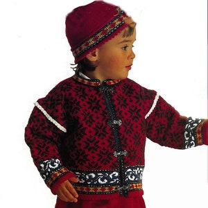 Puede incluir: Un niño lleva un suéter rojo tejido con un patrón blanco y negro, un borde blanco y botones plateados. El suéter tiene una banda con patrón rojo, blanco y azul alrededor de la parte inferior. El niño también lleva un gorro rojo tejido con una banda con patrón negro y dorado.