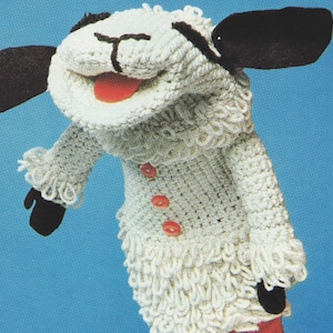 Peut inclure: Marionnette en crochet blanc représentant un mouton avec des oreilles noires et une bouche rouge. Le mouton a trois boutons rouges sur la poitrine et porte une robe en crochet blanc.