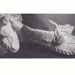 May include: A pair of white knitted slipper socks with a tassel detail. The socks are made with a delicate stitch pattern and have a soft, cosy look.