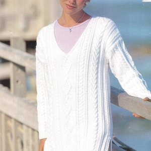 May include: White cable knit jumper with a v-neck and side slits. The jumper is loose fitting and has a relaxed style.