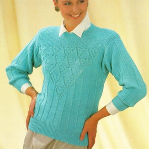 May include: A turquoise knitted sweater with a lacy, diamond-shaped design on the front. The sweater has long sleeves and a round neckline.