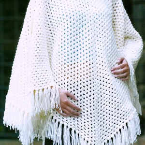Puede incluir: Poncho de crochet blanco con flecos. El poncho está hecho con un patrón de punto de encaje.