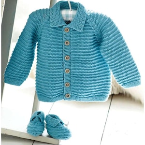 May include: A light blue knitted baby cardigan with a collar and wooden buttons, hanging on a white hanger. Matching knitted baby booties are placed below the cardigan. The cardigan and booties are made of a soft, textured yarn.