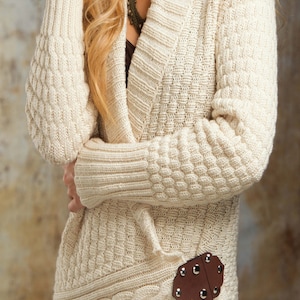 May include: A cream-colored knitted cardigan with a long, open front and a cable knit design. The cardigan has a brown leather patch with metal rivets on the side.