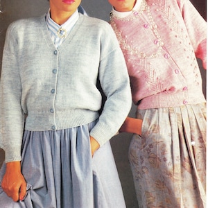 以下が含まれることがあります： カーディガンを着た2人の女性。左の女性は、白い襟付きシャツの下に薄いブルーのカーディガンを着ています。右の女性は、ビーズネックレスと花柄のスカートにピンクのカーディガンを着ています。