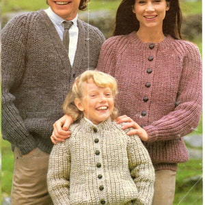 May include: A family wearing knitted cardigans. The father is wearing a brown cardigan, the mother is wearing a pink cardigan, and the child is wearing a cream cardigan.