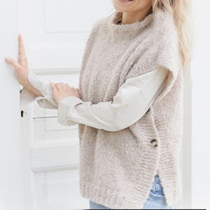 May include: A beige knitted sleeveless sweater with a high neck and a single button on the side.