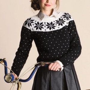 Op de afbeelding: Een zwart-witte trui met een sneeuwvlokkenpatroon op de halslijn. De trui wordt gedragen door iemand die een fietsstuur vasthoudt.