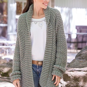 May include: A long, gray cardigan with a shawl collar and long sleeves. The cardigan is made of a soft, textured yarn and has a relaxed fit.