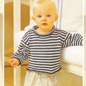 May include: A toddler wearing a striped blue and white knitted sweater. The sweater has a round neckline and long sleeves.