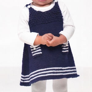 Pode incluir: Uma criança pequena vestindo um vestido de tricô azul e branco listrado com meias brancas e tênis pretos.