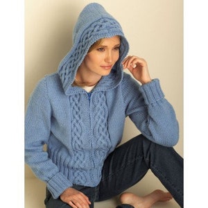 May include: A light blue hooded sweater with a cable knit design. The sweater has a zipper closure and ribbed cuffs. The hood features a decorative cable knit pattern. The model is wearing dark blue jeans.