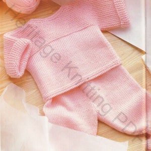Op de afbeelding: Een roze gebreide baby-outfit met een longsleeve trui en broek.