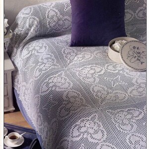 Peut inclure: Une couvre-lit blanche en crochet avec un motif floral délicat. Un oreiller violet et une boîte blanche avec des fleurs blanches sont sur la couvre-lit.